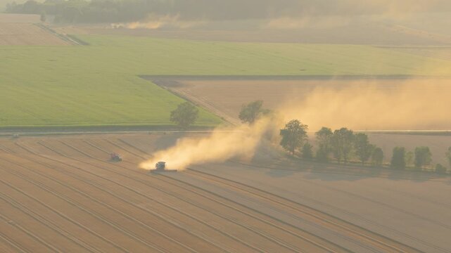 Combine harvester raising dust during sunset harvest