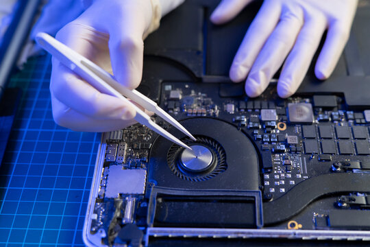A person is cleaning the inside of a laptop using tweezers and gloves at a workspace
