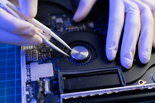Person uses tweezers to clean the inside of a laptop in a workspace with blue lighting
