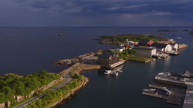 Aerial view shows modern and traditional buildings, a marina with docked boats, and a coastal road on an island peninsula in Lofoten, Norway.