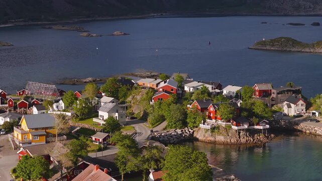 Aerial view of traditional rorbuer wooden houses, fish drying racks, and water along the coastline in Lofoten, Norway on a bright day.
