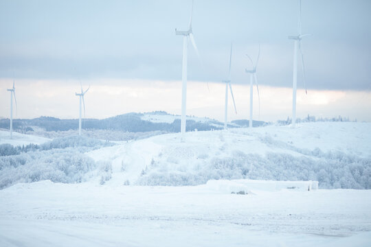 Wind turbines stand tall on a snow-covered hill under a cloudy sky