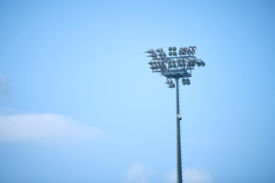 Stadium floodlights rise against a blue summer sky