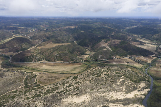Aerial view of rolling hills, a winding river, and sand dunes in the rural landscape of Portugal.