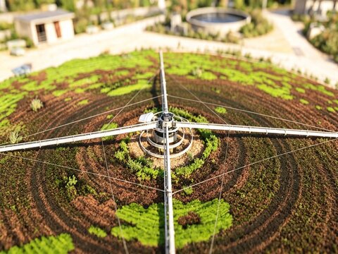 Aerial view of Raunds Water Recycling Centre featuring a circular trickling filter with rotating arms and patterned vegetation in Raunds, England, United Kingdom.