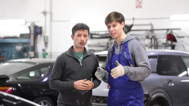Guy car mechanic talks with man client in workshop and takes order. Customer explains details of order to contractor and talks about problem with car.