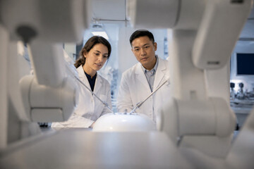 Fototapeta premium Two scientists in white coats inspect advanced robotics in a modern laboratory, focusing on a glowing central chamber. Concept of research, technology, and innovation in engineering.