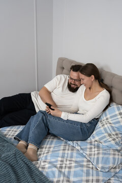 Couple scrolling on a smartphone together, enjoying leisure time in bed, showcasing a modern relationship connected through technology and digital activities at home. Vertical photo