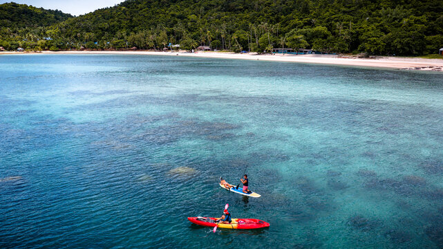 Top aerial view of Group of tourist are enjoy on water sport paddle sup-board with kayaking along at the edge of the sea beach under crystal clear of water in the island of summer trip