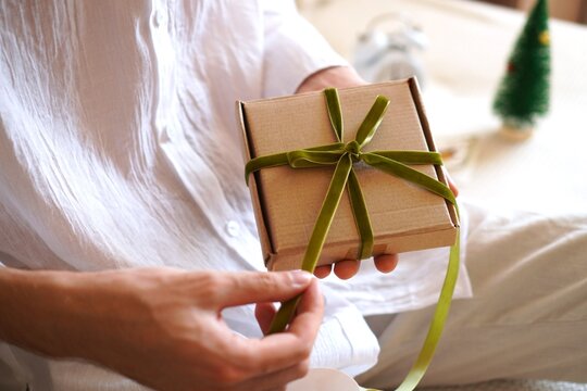 A man untying a green ribbon on a craft gift box. Express holiday gift delivery service, Christmas or birthday surprise. Unboxing a package, receiving online order, and cozy festive atmosphere