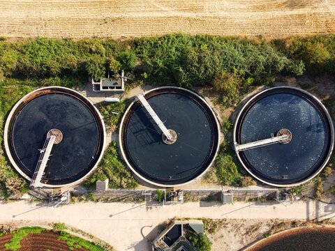 Aerial view of Raunds Water Recycling Centre featuring three large circular sedimentation tanks with rotating bridges surrounded by green vegetation in Raunds, England, United Kingdom.