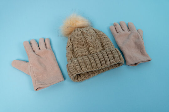 Knit hat and gloves arranged on a light blue surface for winter wear