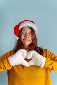 Woman in Santa hat shows heart shape with gloves on blue background