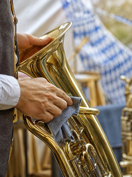 Man polishing brass tuba at Oktoberfest festival. Traditional bavarian brass band instrument preparation for folk music celebration. German culture and autumn beer festival concept