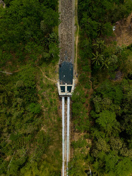 Aerial view of the Talangagung Metro Syphon, a concrete structure with large pipes transporting water through a lush green landscape in Malang, East Java, Indonesia.