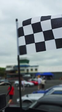 Checkered flag waves over race cars and fans. vertical video