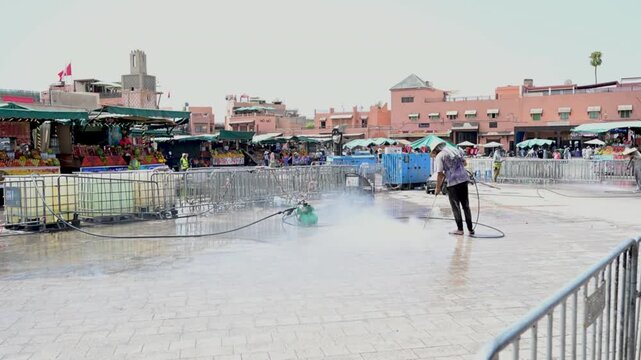Marrakech, morocco. August 8, 2026. Street cleaner using a high pressure washer to clean the stone pavement in djemaa el fna square, with the medina souk in the background
