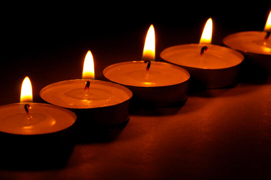 Row of lit tea light candles glowing warmly in the dark