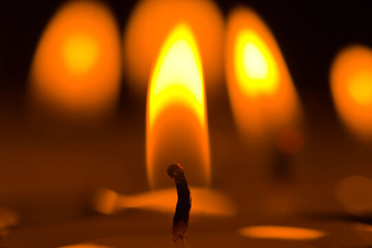 Close-up of a single candle flame burning brightly in the dark with bokeh effect