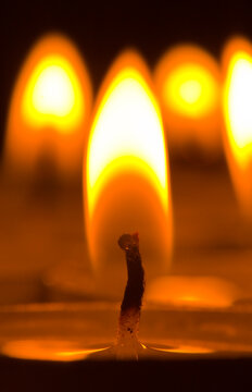 Close-up of a single candle wick burning with multiple flames in the background