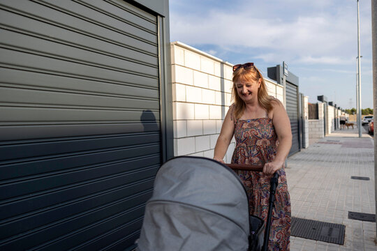 Smiling woman pushing baby stroller walking on sidewalk