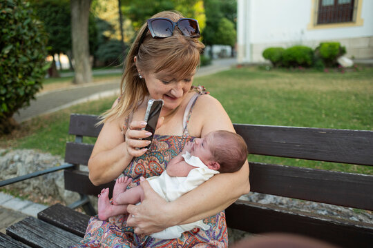 Grandmother recording newborn baby in park with smartphone
