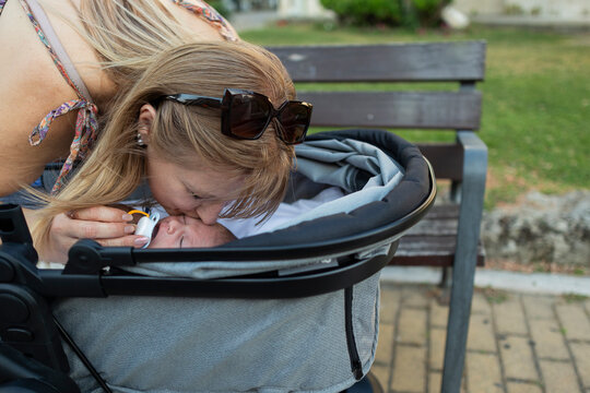 Mother tenderly kissing baby in stroller outdoors