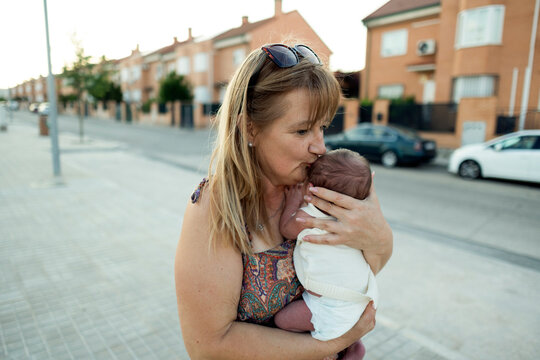 Woman tenderly kissing baby on outdoor street