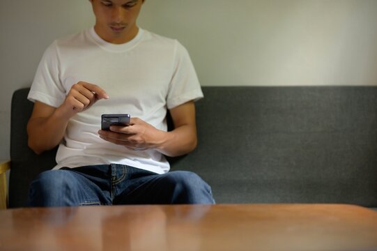 Young Man Using Smartphone While Sitting on Gray Couch Indoor