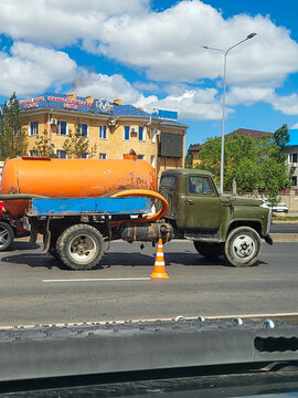 A green GAZ-53 vacuum truck with an orange tank body is parked on a city street in front of residential buildings in Astana; a classic Soviet truck, capital city, Kazakhstan 20.05.2025
