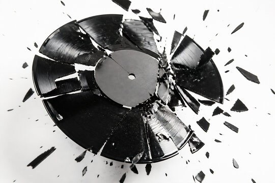 A black vinyl record is shattered into many pieces on a white surface.