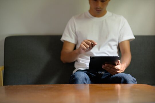 Young Man Using Tablet While Sitting on Couch in Casual Attire