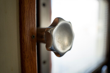 Close up of vintage silver metal adjustment knob handle on wooden frame in ship bridge interior, showing mechanical hardware detail. © Marina