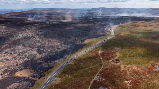 Burnt moorland and smoke whirl on Llangynidr Moors, Brecon Beacons, charred earth contrasting with unburnt grassland beside a scenic mountain road in Wales