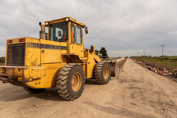 Fototapeta premium Yellow wheel loader parked on the shoulder of a highway construction site