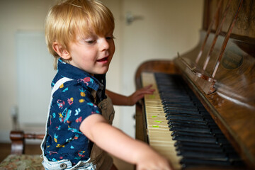 Young child playing a piano with a focused expression indoors. © Rawpixel.com