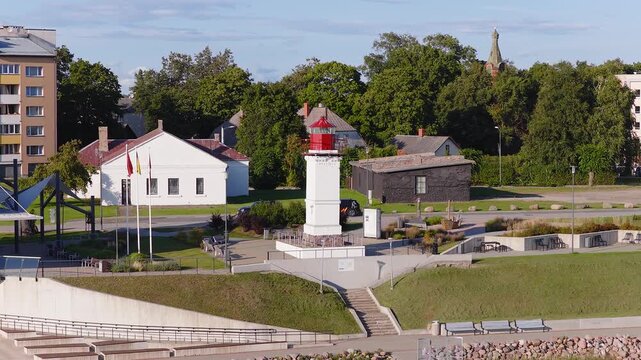 Aerial view showcases the historic lighthouse, promenade, buildings, and trees in the coastal town of Salacgriva, Latvia, in daylight.