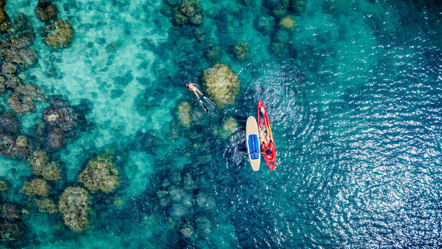 Top aerial view of Group of tourist are enjoy on water sport paddle sup-board with kayaking along at the edge of the sea beach under crystal clear of water in the island of summer trip