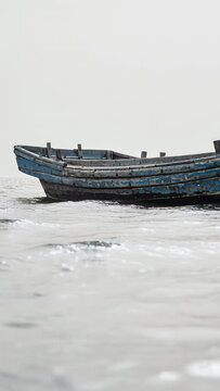 Vertical video: Bobbing weathered blue rowboat floating on calm water, driven by gentle ripples