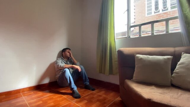 A young Hispanic man sits on the floor, appearing bored, depressed, and discriminated against within his home in Bosa, Bogot&aacute;, Colombia. Concept of suicide and mental health