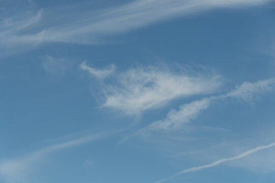 Soft white cirrus clouds spreading across clear blue sky creating a peaceful natural background texture