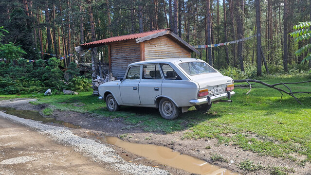 White IZH-2125 hatchback-wagon at the edge of the forest in front of a wooden house in Elekmonar, a vintage Soviet IZH wagon from the 1970s, Altai Republic, Siberia, Russia 02.08.25