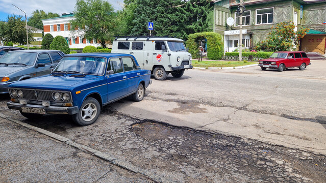 Blue Lada VAZ-2106 sedan, UAZ-452 "Bukhanka" minibus, and red Lada 2104 station wagon in street traffic in Rodino; a scene of everyday Russian life, Altai Region, Siberia, Russia 10.08.2025