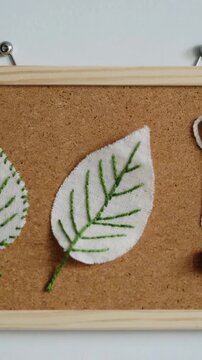 Vertical video: Zooming camera centering white felt leaf on cork board to reveal green veins