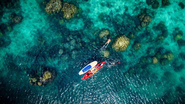 Top aerial view of Group of tourist are enjoy on water sport paddle sup-board with kayaking along at the edge of the sea beach under crystal clear of water in the island of summer trip