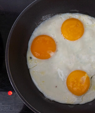 Three fried eggs in a black frying pan