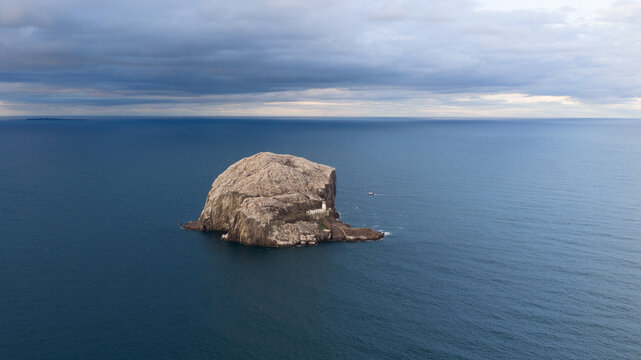 Aerial view of Bass Rock, a volcanic island in the Firth of Forth featuring a historic lighthouse, surrounded by deep blue sea under a cloudy sky in Scotland, United Kingdom.