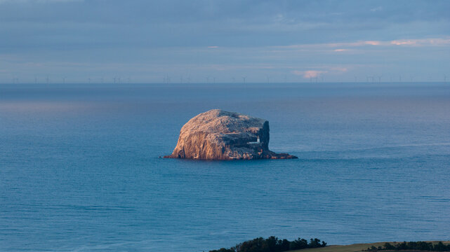 Aerial view of Bass Rock rising from the North Sea with a distant wind farm on the horizon in Scotland, United Kingdom.