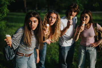 Fototapeta premium Teenagers eating ice cream cones together in a green park. A group of friends share a playful summer moment outdoors.