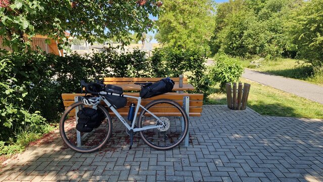 Cube Nuroad Ex gravel bike with bikepacking bags parked next to a wooden bench at a rest area in a green setting; a break during a bike ride in sunny summer weather, Germany Ochsenfurt 13.05.2026
